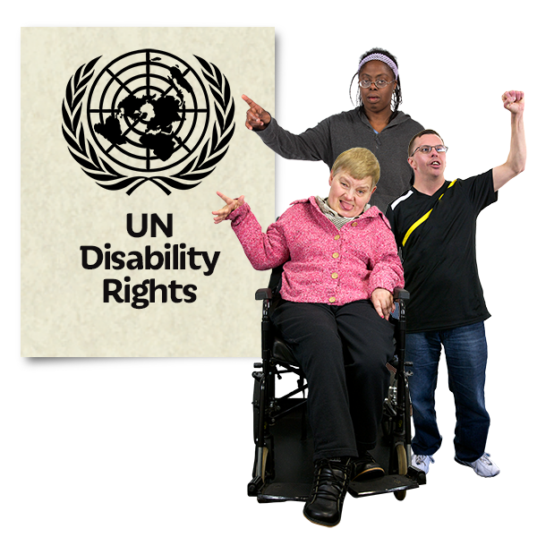 Three people together each holding one had in the air. They stand and sit beside a sign that reads "UN Disability Rights"
